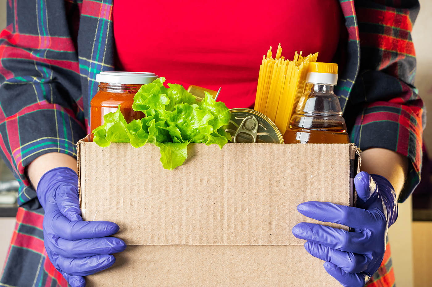 A young woman volunteer is holding a donation box with foodstuffs. Delivery of necessary food during an epidemic.